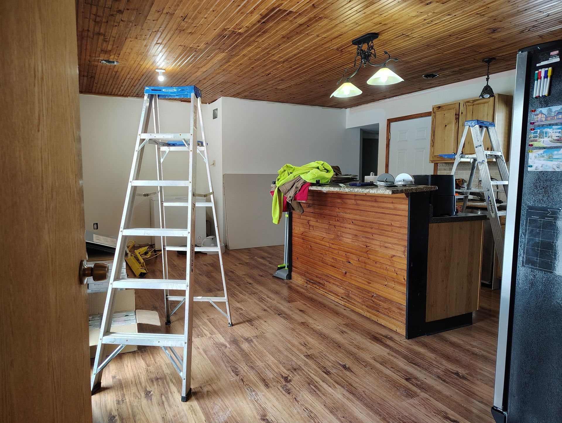 Kitchen under renovation with ladders, wood ceiling, and new flooring.