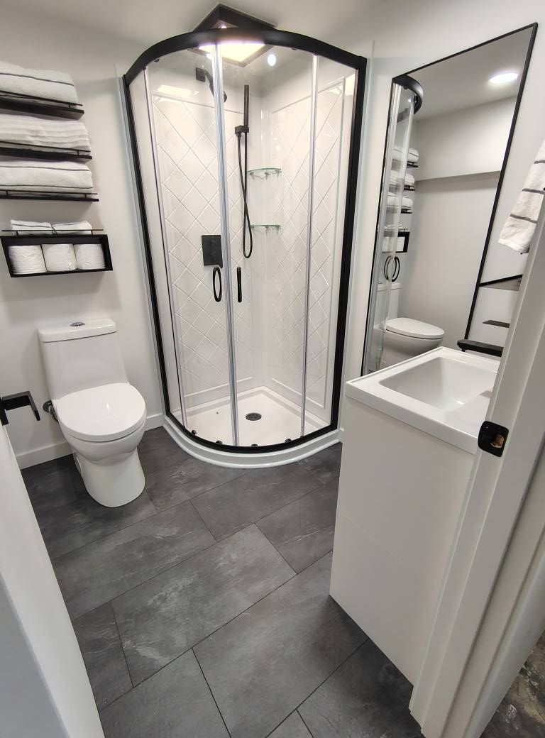 Modern bathroom with a glass shower, toilet, and vanity with dark gray flooring and white walls.