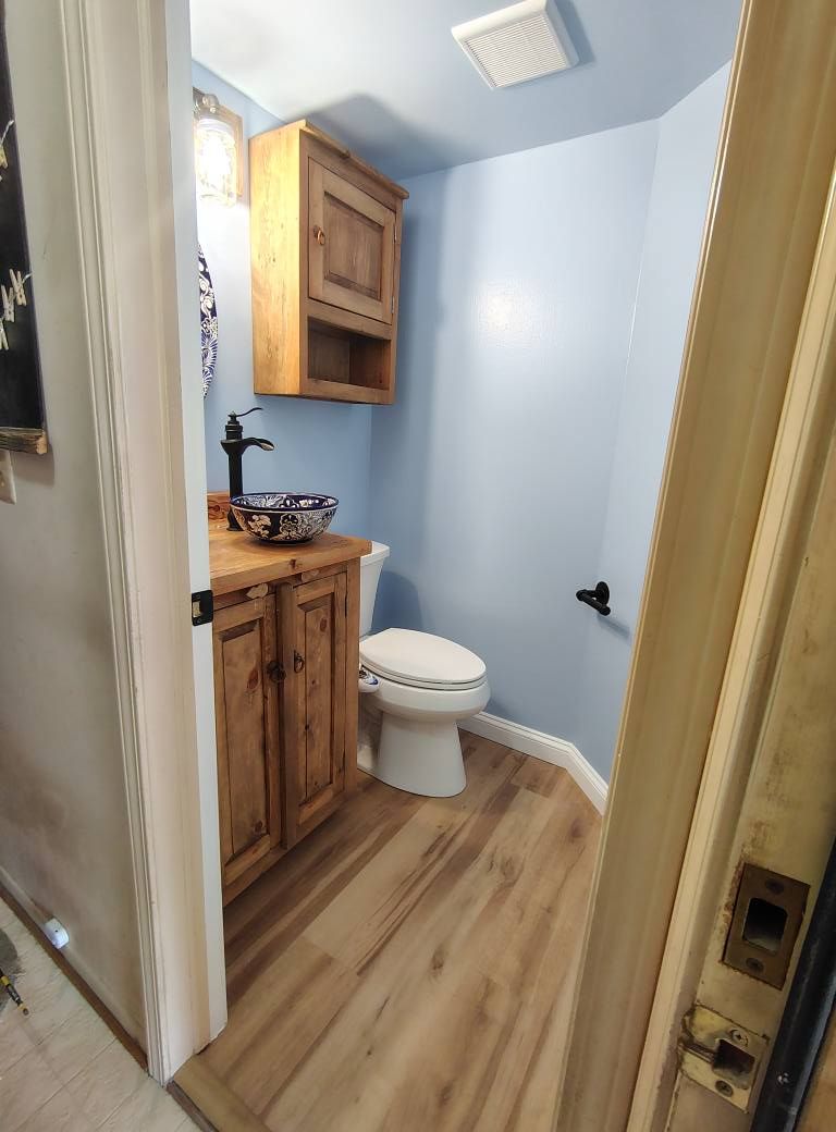 Small powder room with blue walls, wood vanity and flooring, and a white toilet.