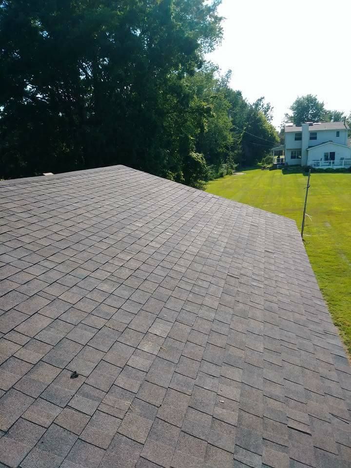 Brown shingle roof with a green lawn and trees in the background under a bright sky.