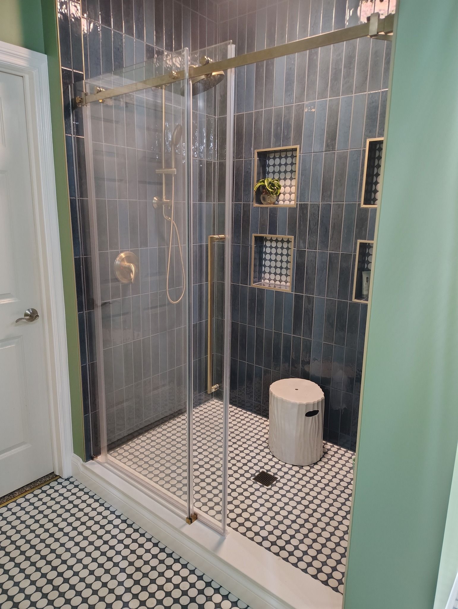 Modern shower with black tiled walls, glass doors, and black/white tiled floor.