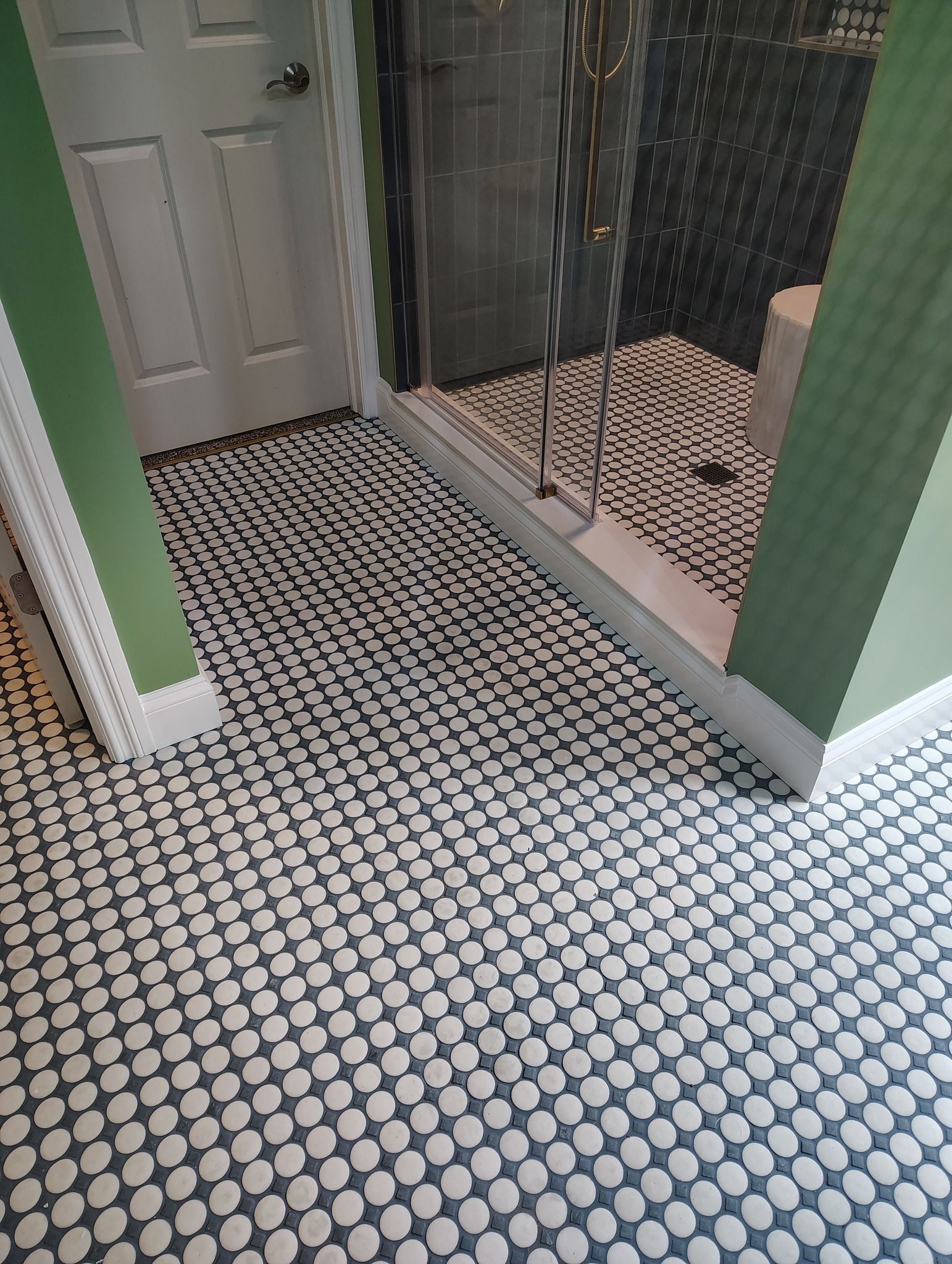 Bathroom with penny tile floor and green walls. A glass shower is visible.