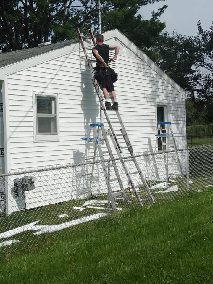 Person on a ladder against a white house, with a second ladder propped beneath it.