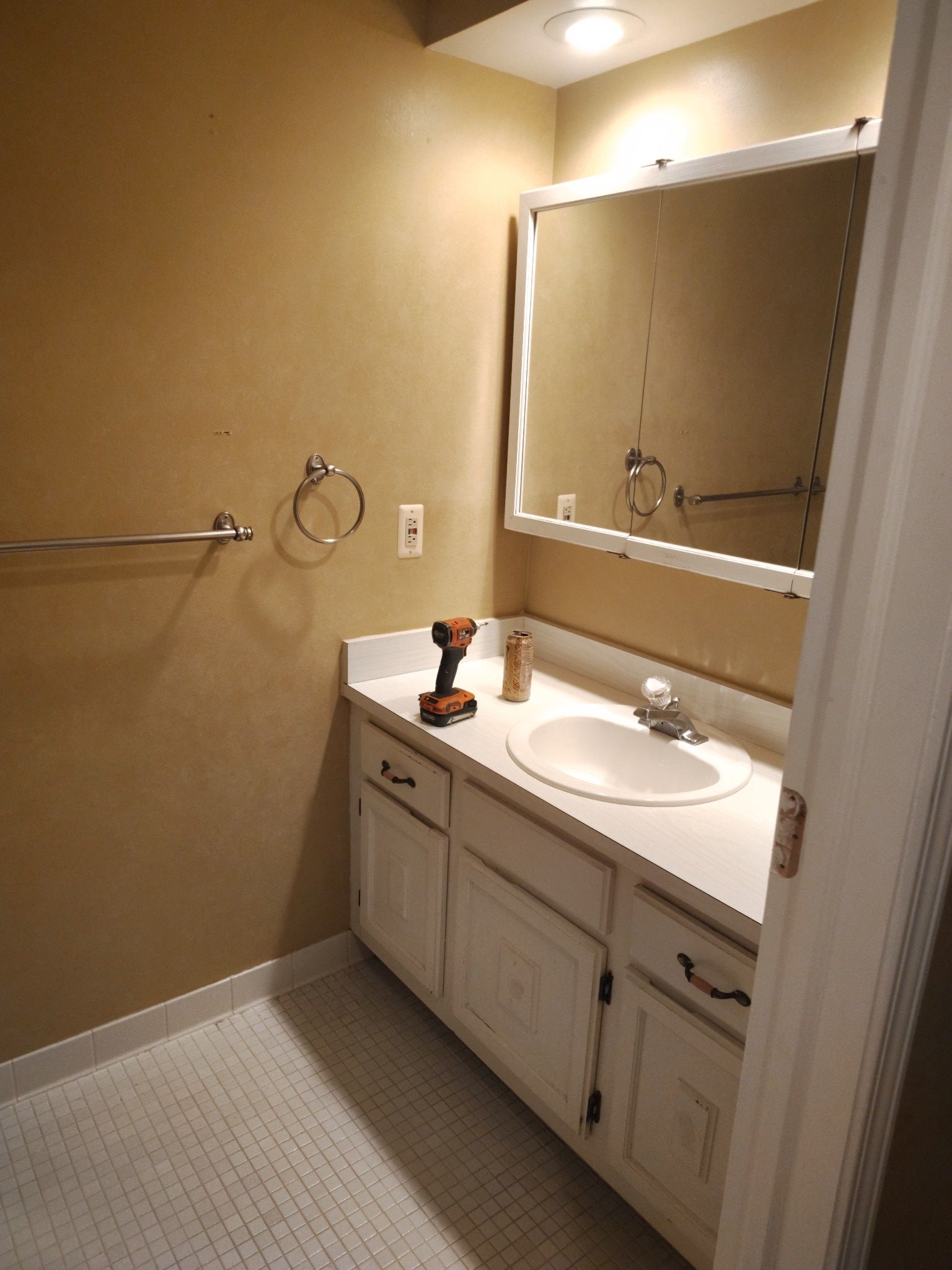 Bathroom with white vanity, mirror, and sink. Wall is tan, with a chrome towel rack.