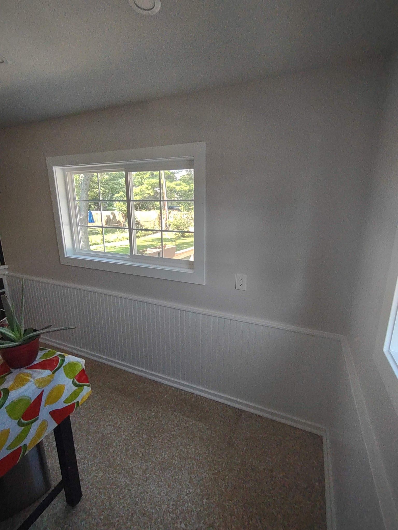 Interior view of a room with a window, white wainscoting, and a table with a patterned tablecloth.