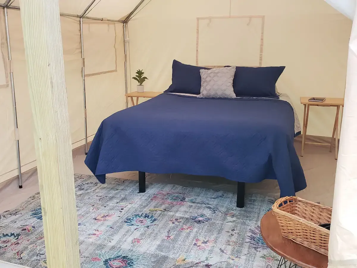 Blue bed in a tent-like room with a patterned rug, small table, and wicker basket