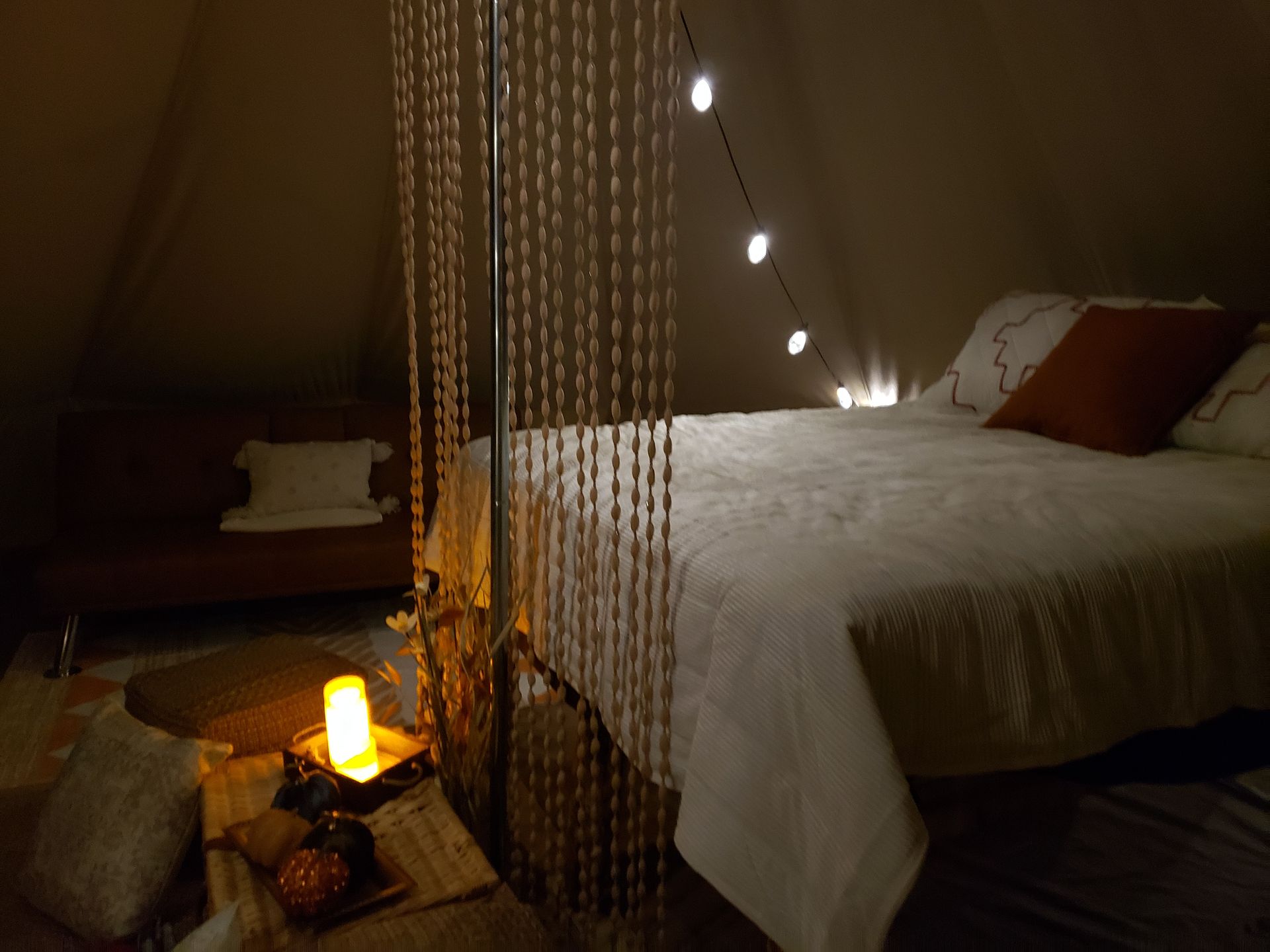 Cozy tent bedroom with a bed, hanging lights, beaded curtain, and glowing lantern at night
