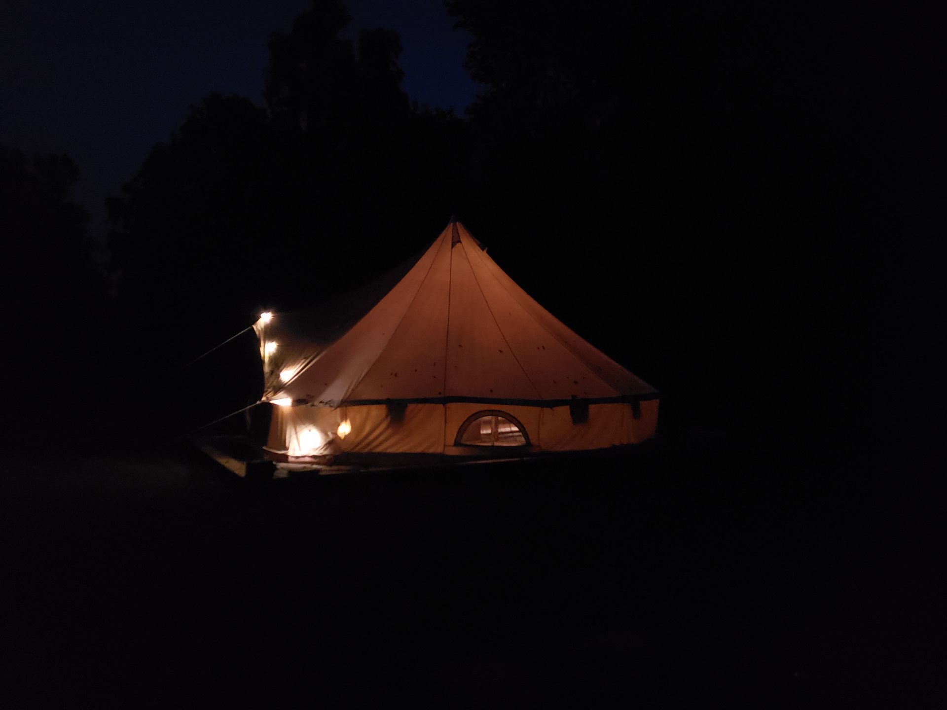 Lit-up orange tent at night in a dark outdoor campsite