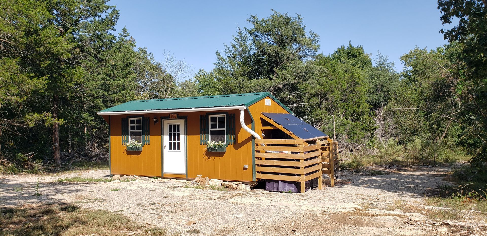 Small orange cabin with a green roof and wooden porch in a wooded clearing.