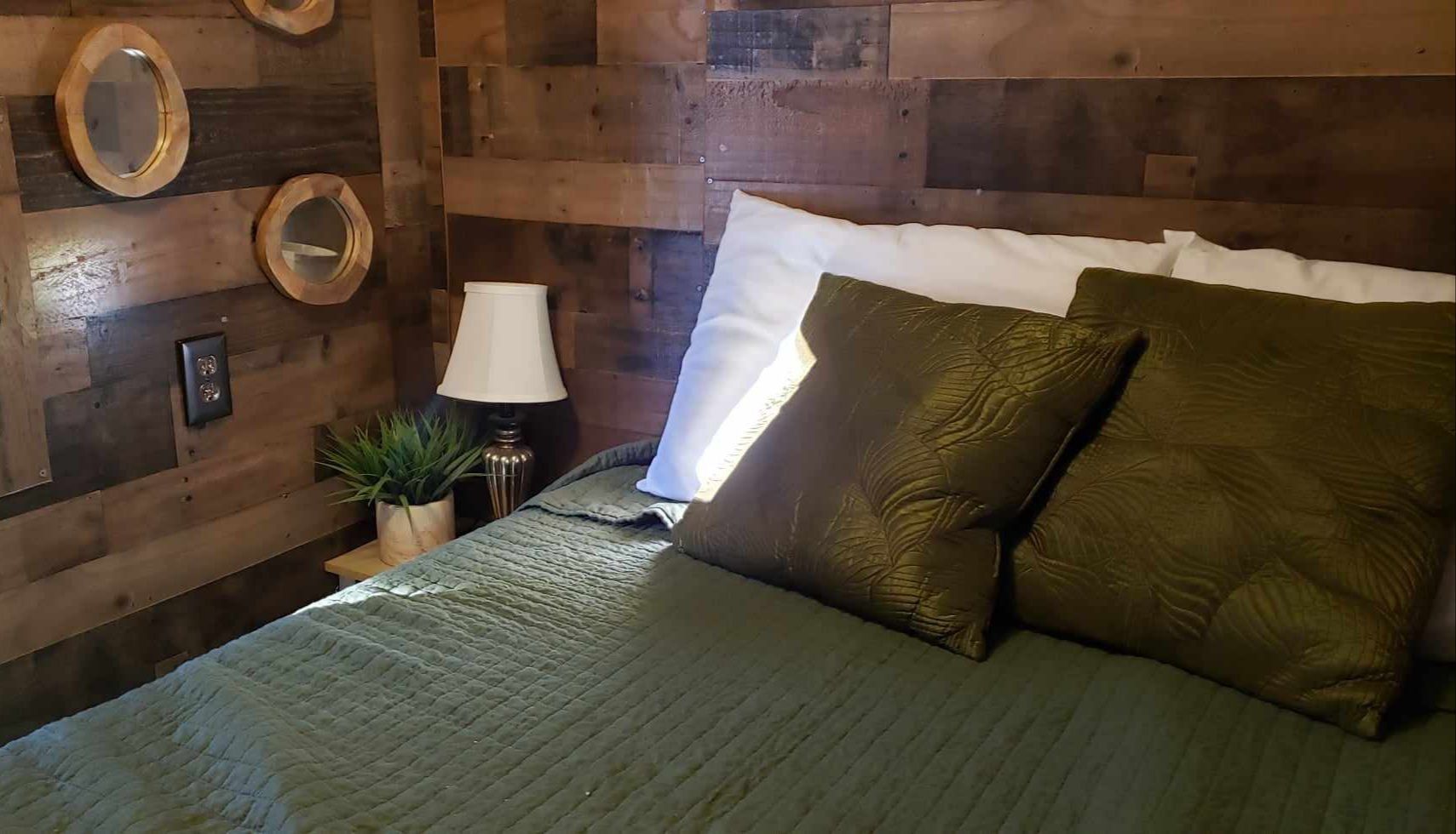 Cozy bedroom with a wooden wall, green bedding, and a bedside lamp with a potted plant.