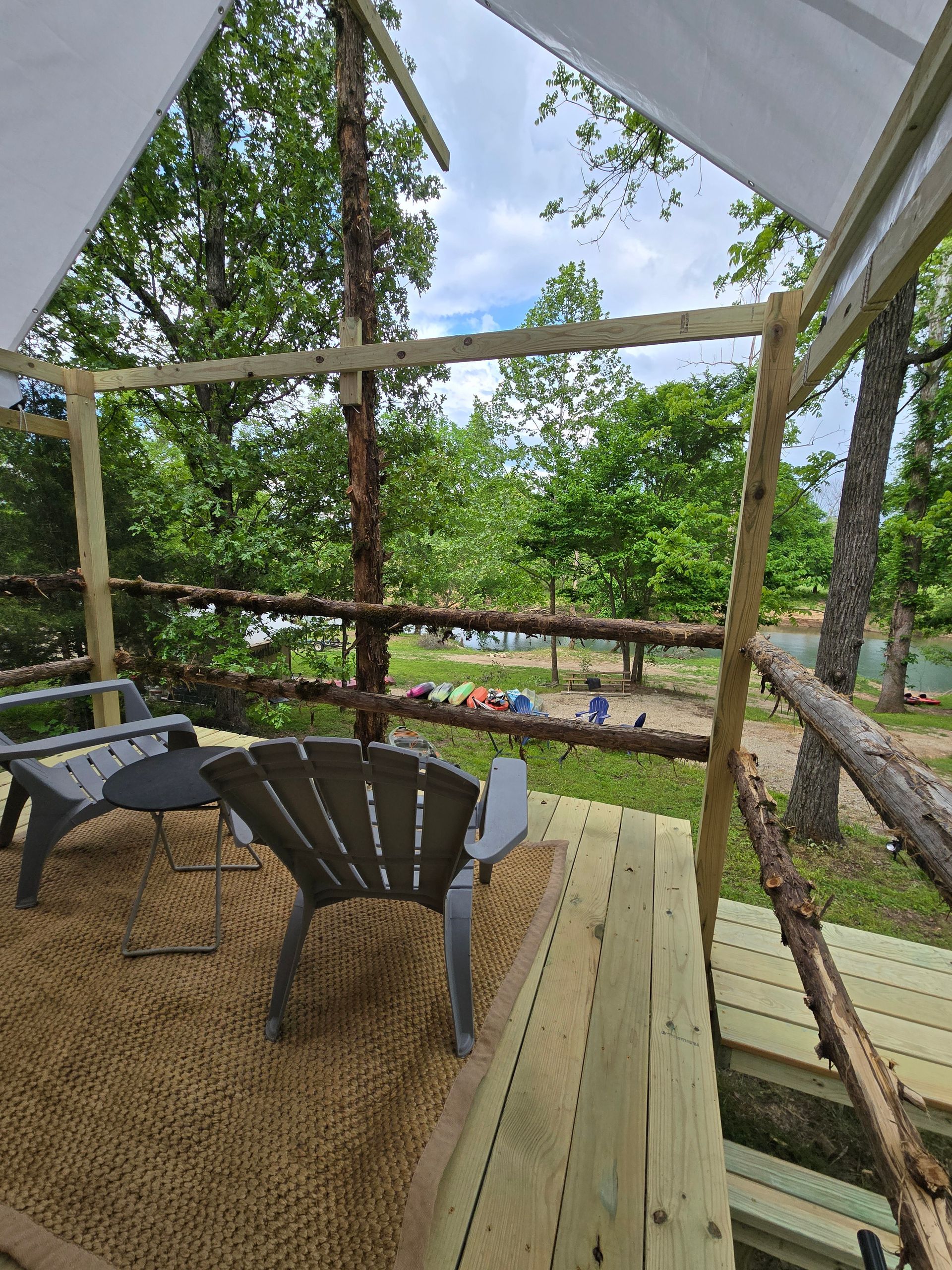 Porch view of a backyard with chairs, wooden steps, and trees beyond a sandy yard.