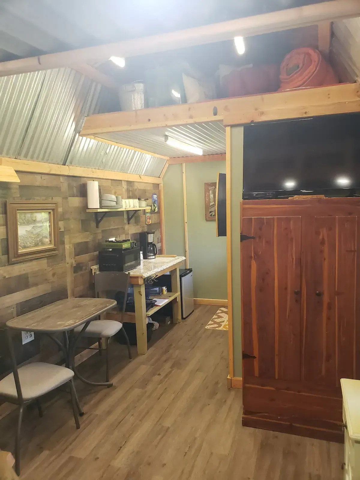 Cozy wood-paneled room with tables, chairs, a shelving unit, and a TV on a cabinet.