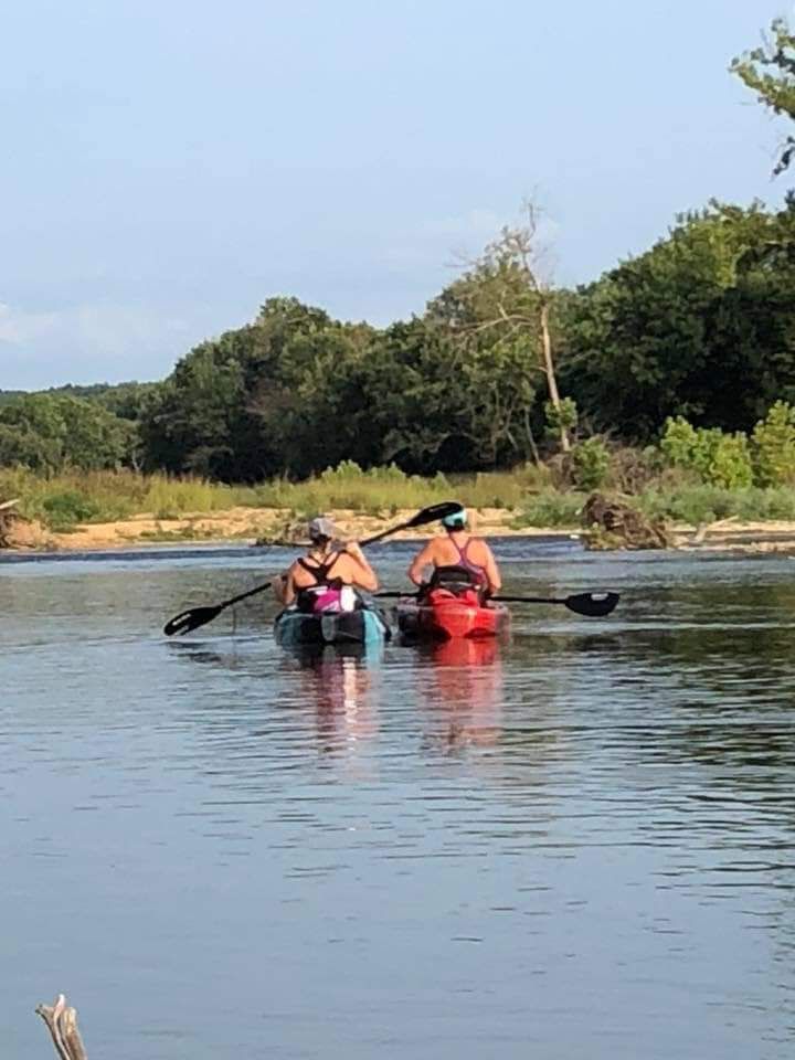Two kayakers paddling on a calm river near a wooded shoreline