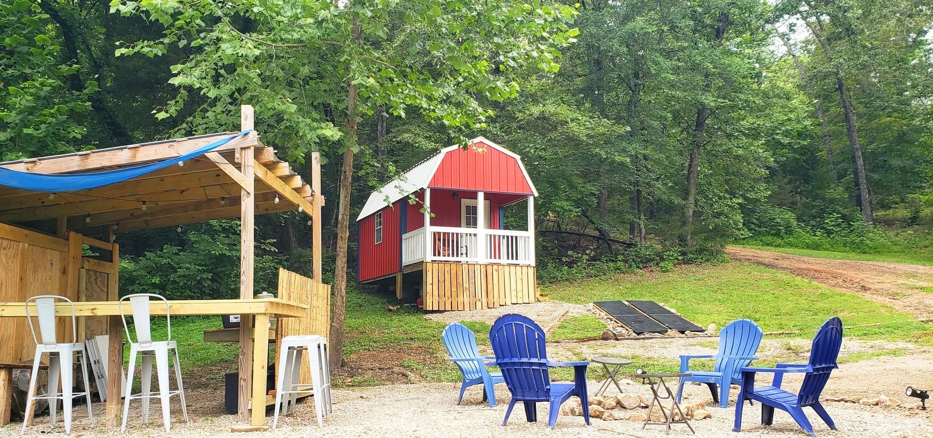 Outdoor campsite with blue chairs, wooden shelter, and a small red-roofed playhouse by trees