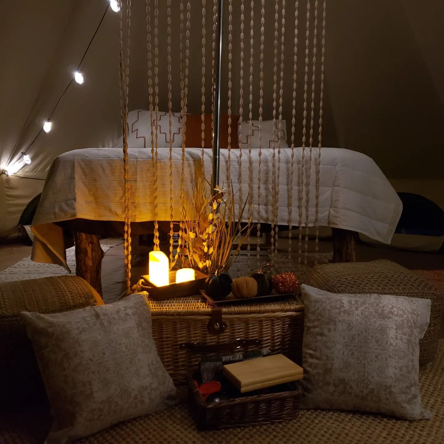 Cozy tent interior with lit candles, string lights, wicker chest, and cushions around a low table