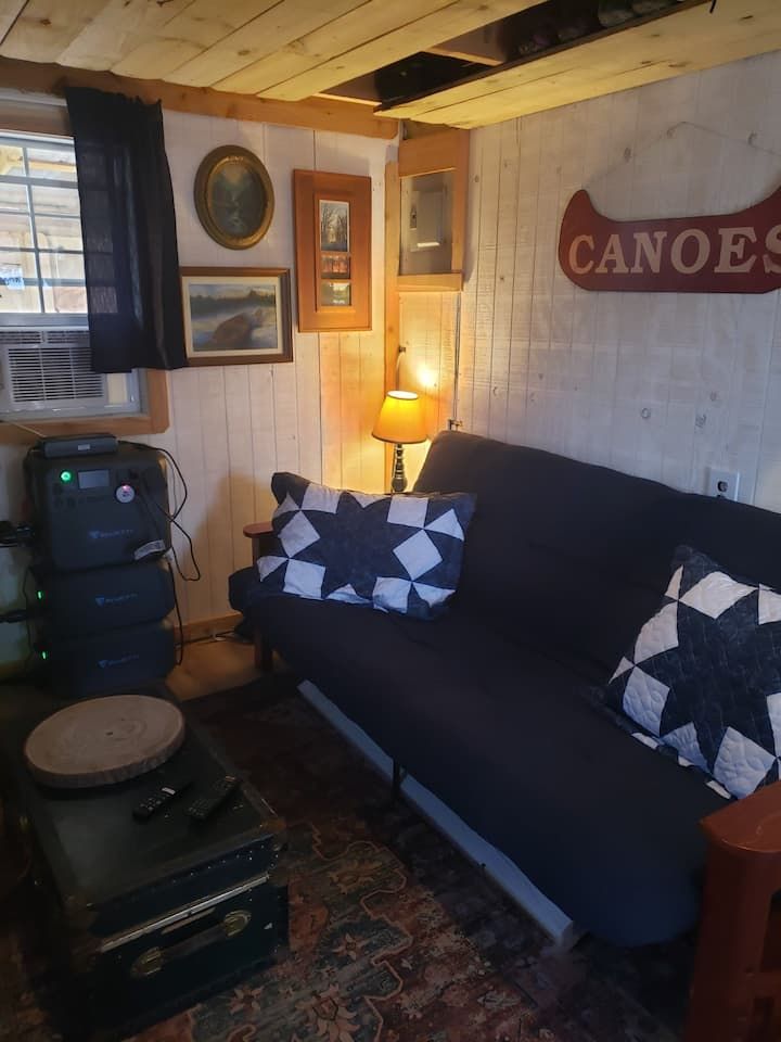 Cozy cabin living room with black couch, patterned pillows, warm lamp, and wooden walls with canoe sign