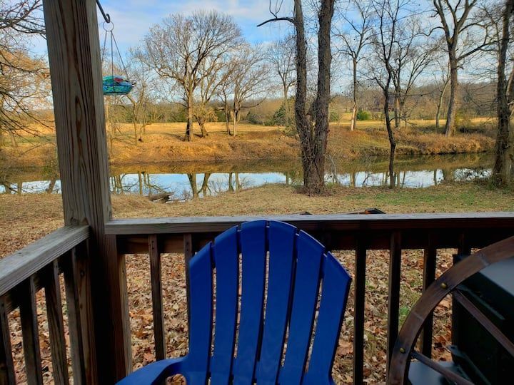 Blue chair on a porch overlooking a calm creek and leafless trees in a sunny rural landscape