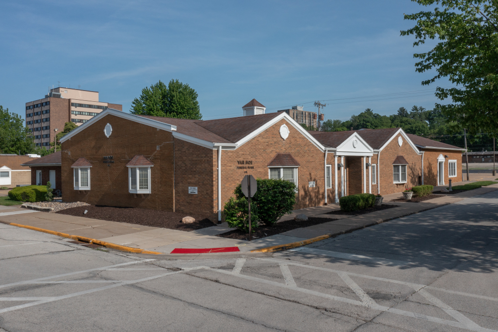 Brick building with white trim and brown roof, situated at a corner. Clear sky.