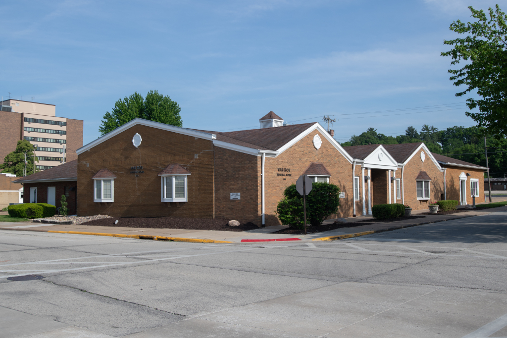 Brick building with brown roof, small windows, and surrounding parking lot under a blue sky.