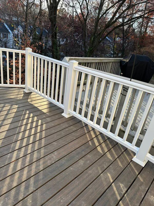 A white railing on a wooden deck with trees in the background.