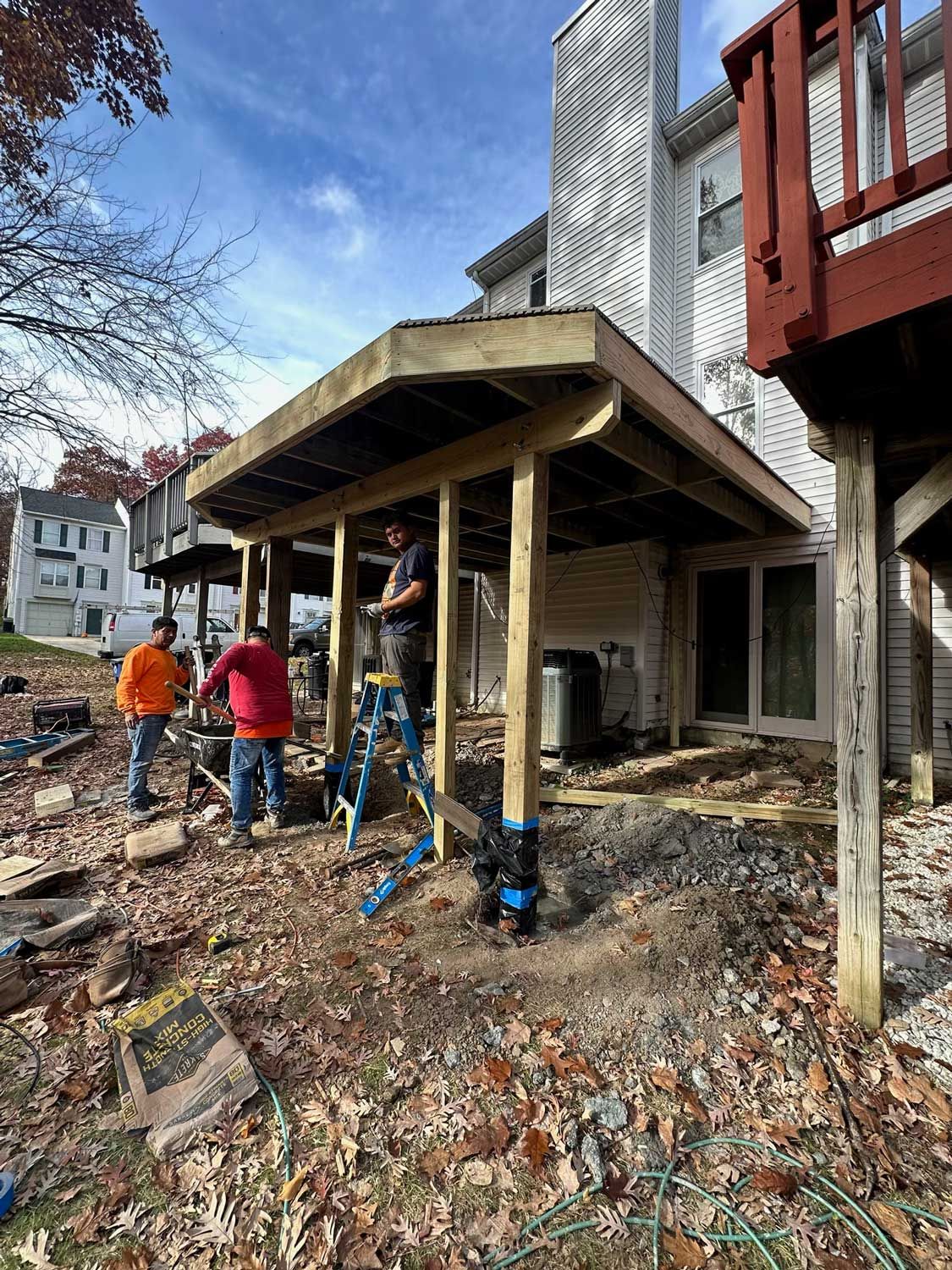 A group of people are working on a wooden deck in front of a house.