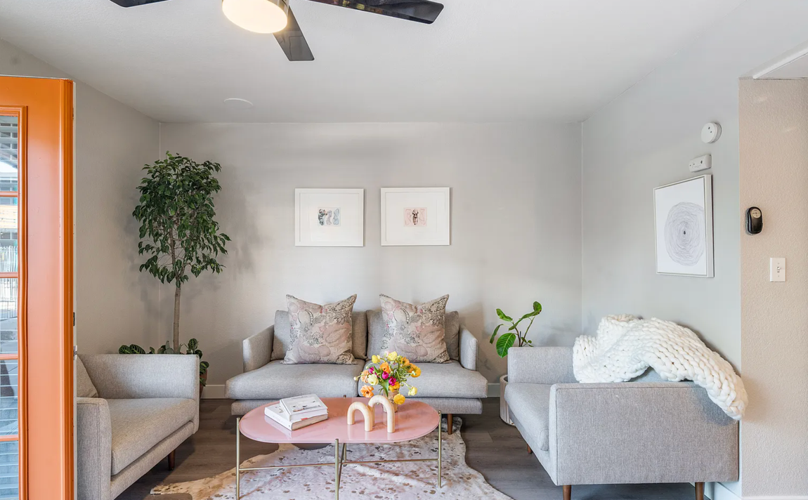 Living room with grey furniture, pink coffee table, artwork, and orange door.