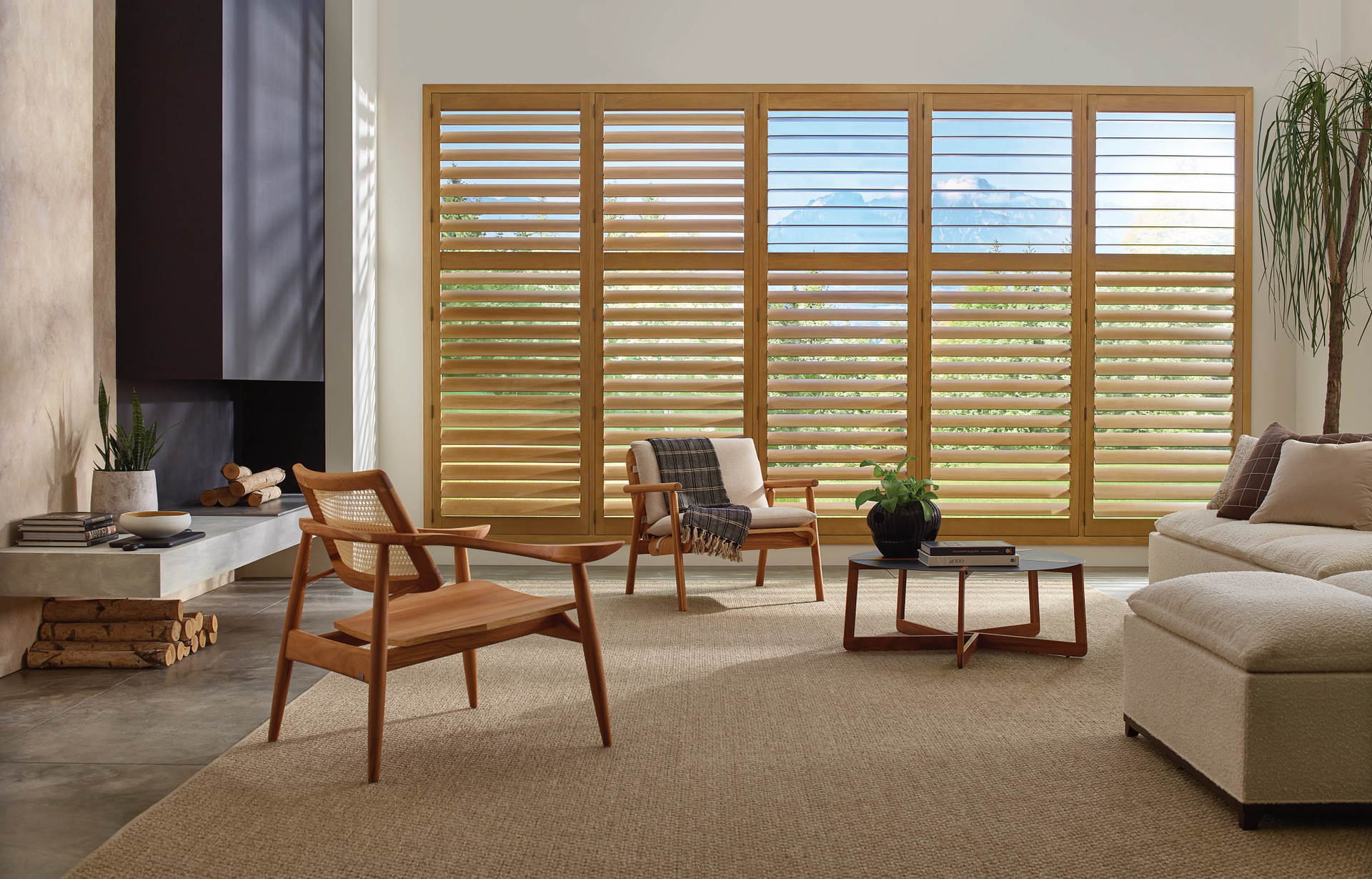Modern living room with large window blinds, wooden chairs, beige sofa, and coffee table