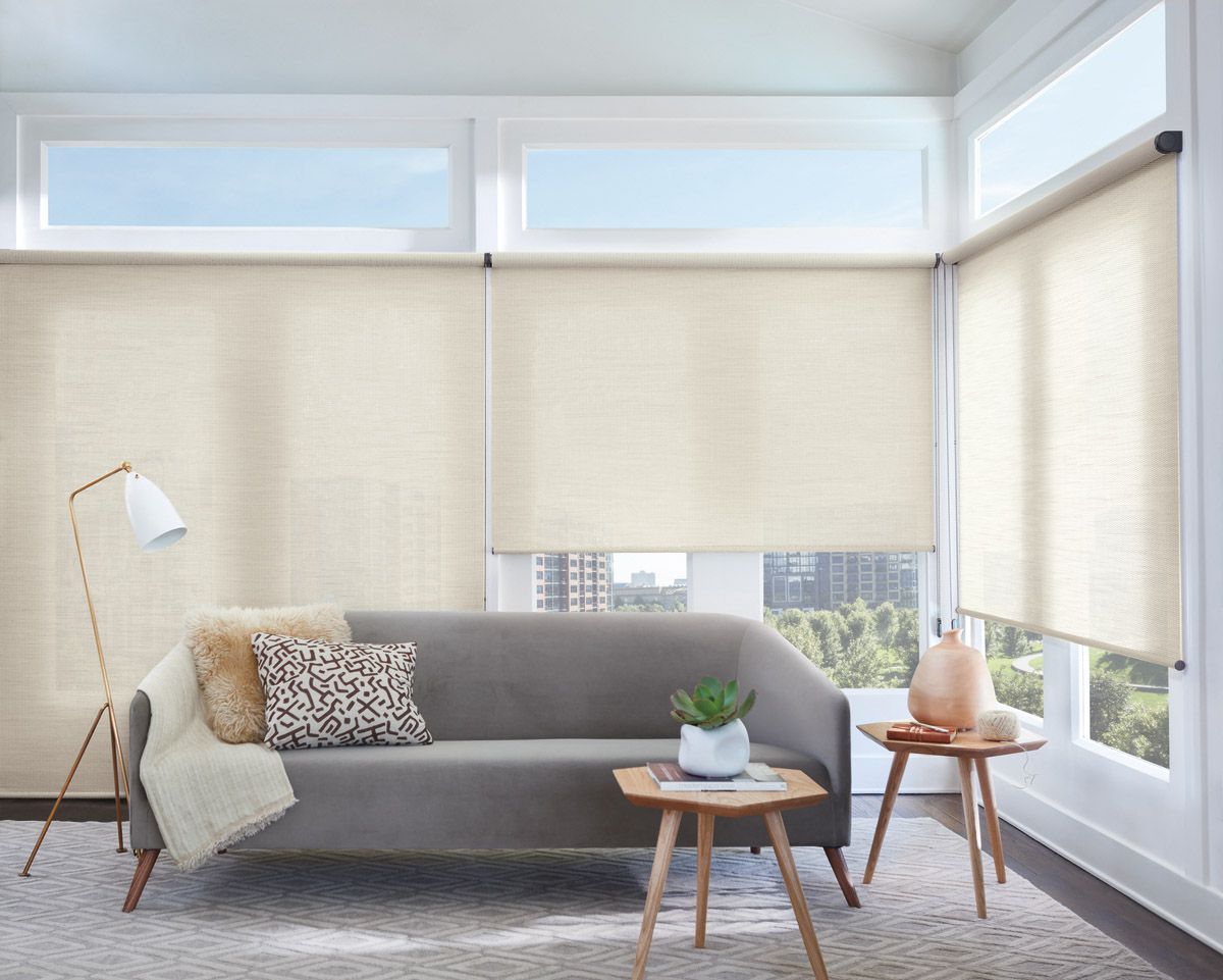 Bright modern living room with a gray sofa, beige blinds, floor lamp, and small wooden tables by large windows