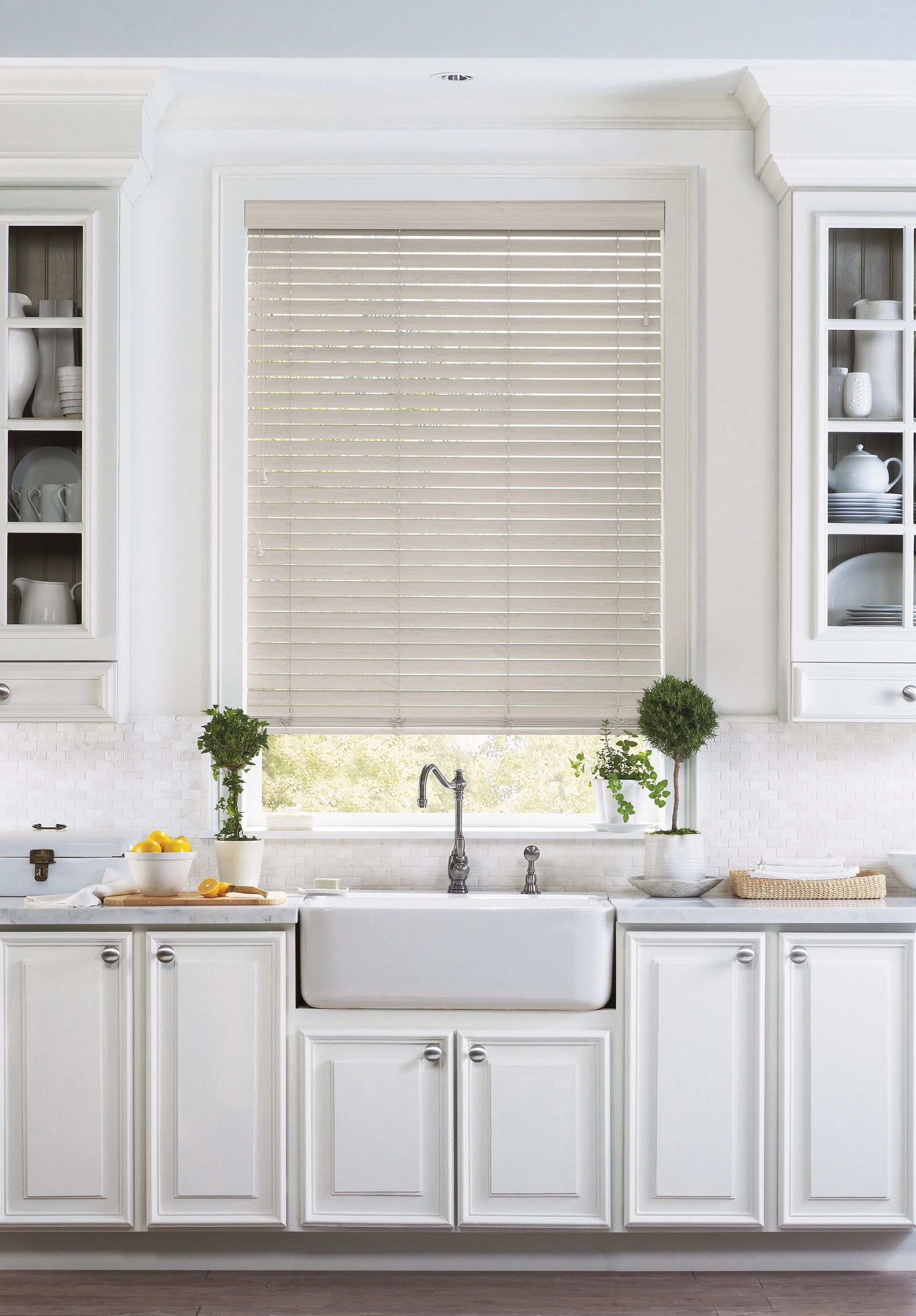 Bright white kitchen with farmhouse sink, beige blinds, and potted plants on the windowsill
