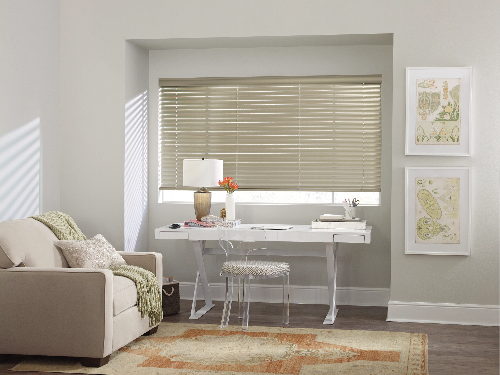 Bright home office nook with white desk, chair, window blinds, framed art, and beige armchair by a rug