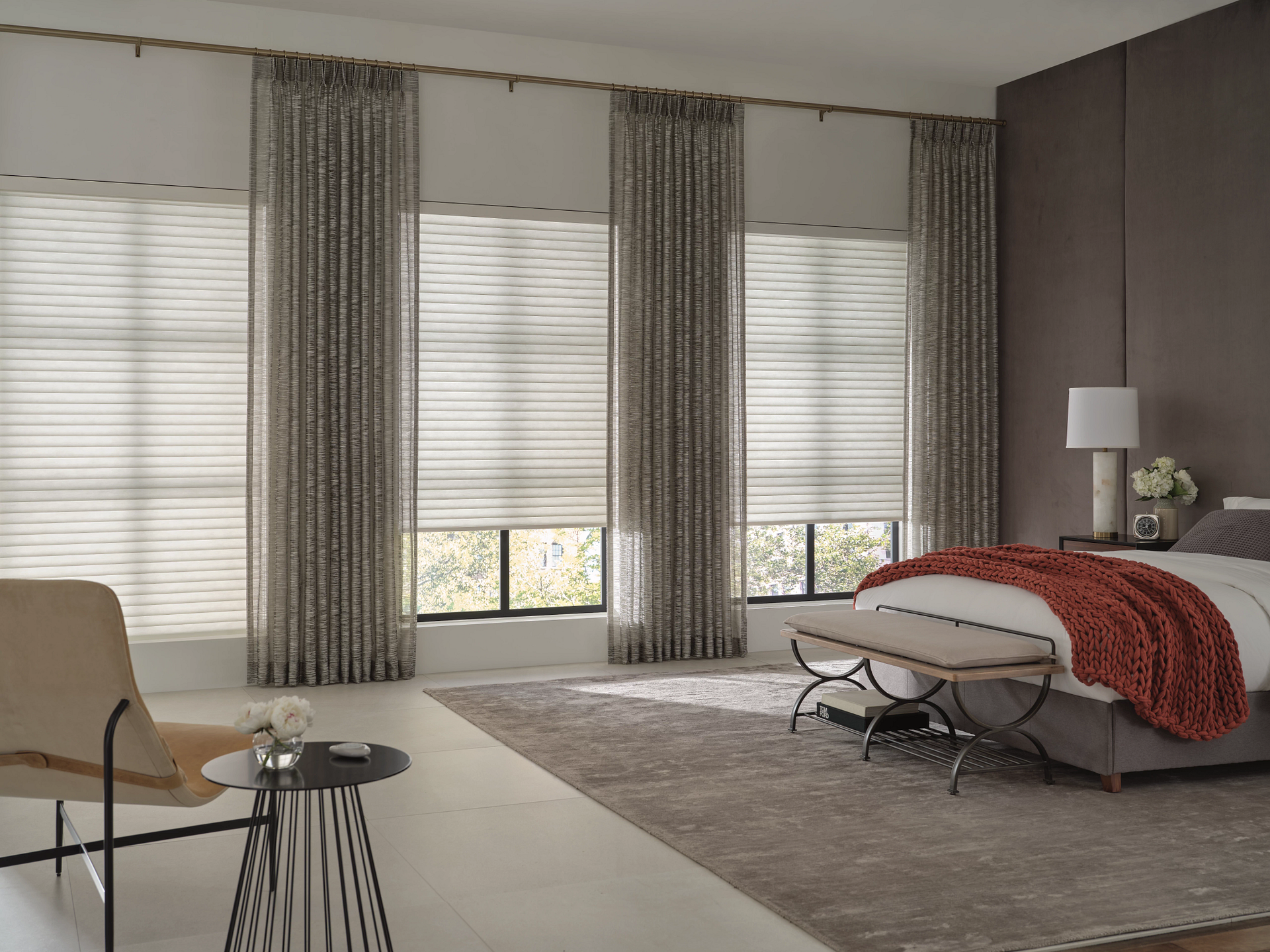 Modern bedroom with large windows, gray curtains, upholstered bed, bedside lamp, and beige rug
