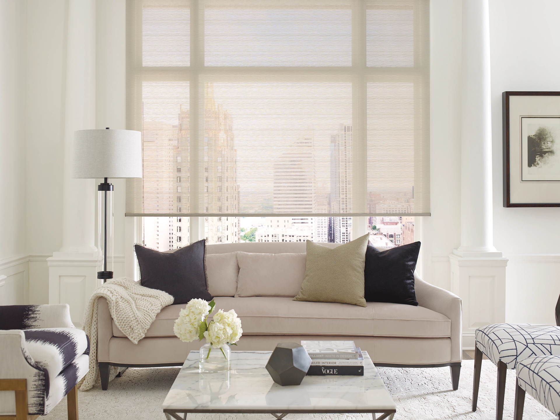 Bright living room with beige sofa, lamp, coffee table, and large window with blinds.