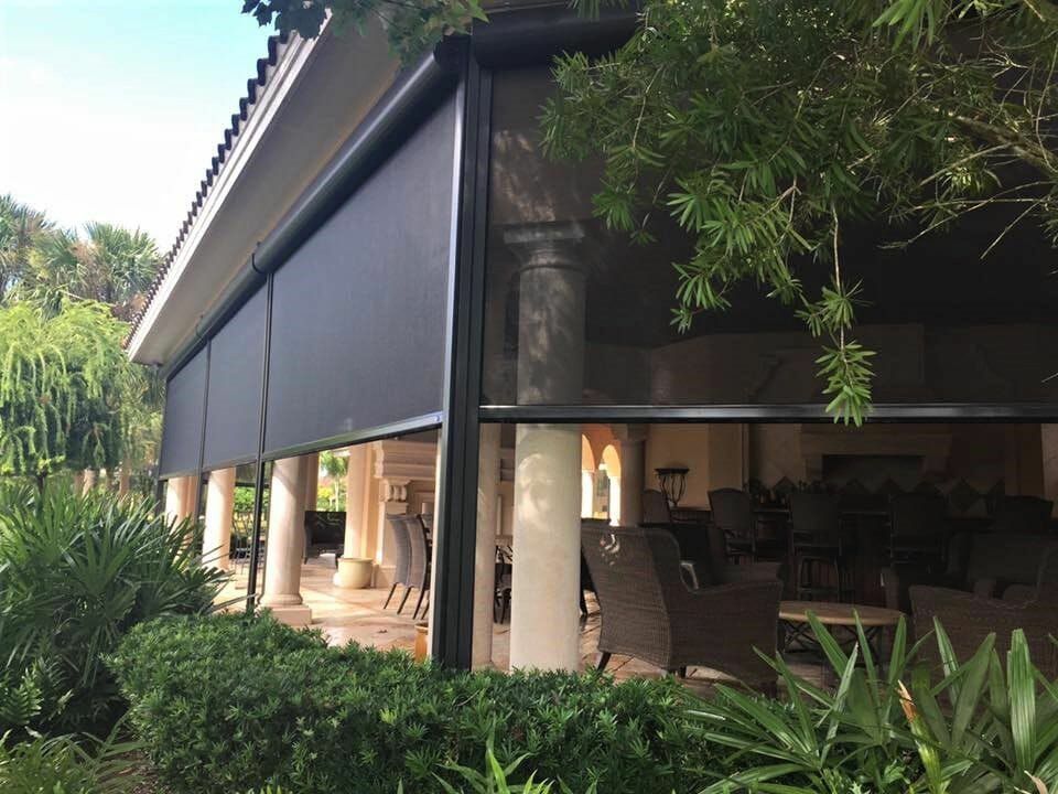 Open-air patio with rolled-down dark awnings, columns, and lush tropical greenery around a shaded seating area