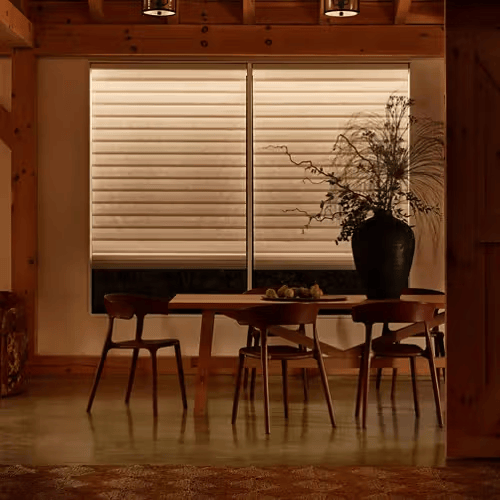 Cozy dining room with wooden table, chairs, large vase, and closed blinds in warm light