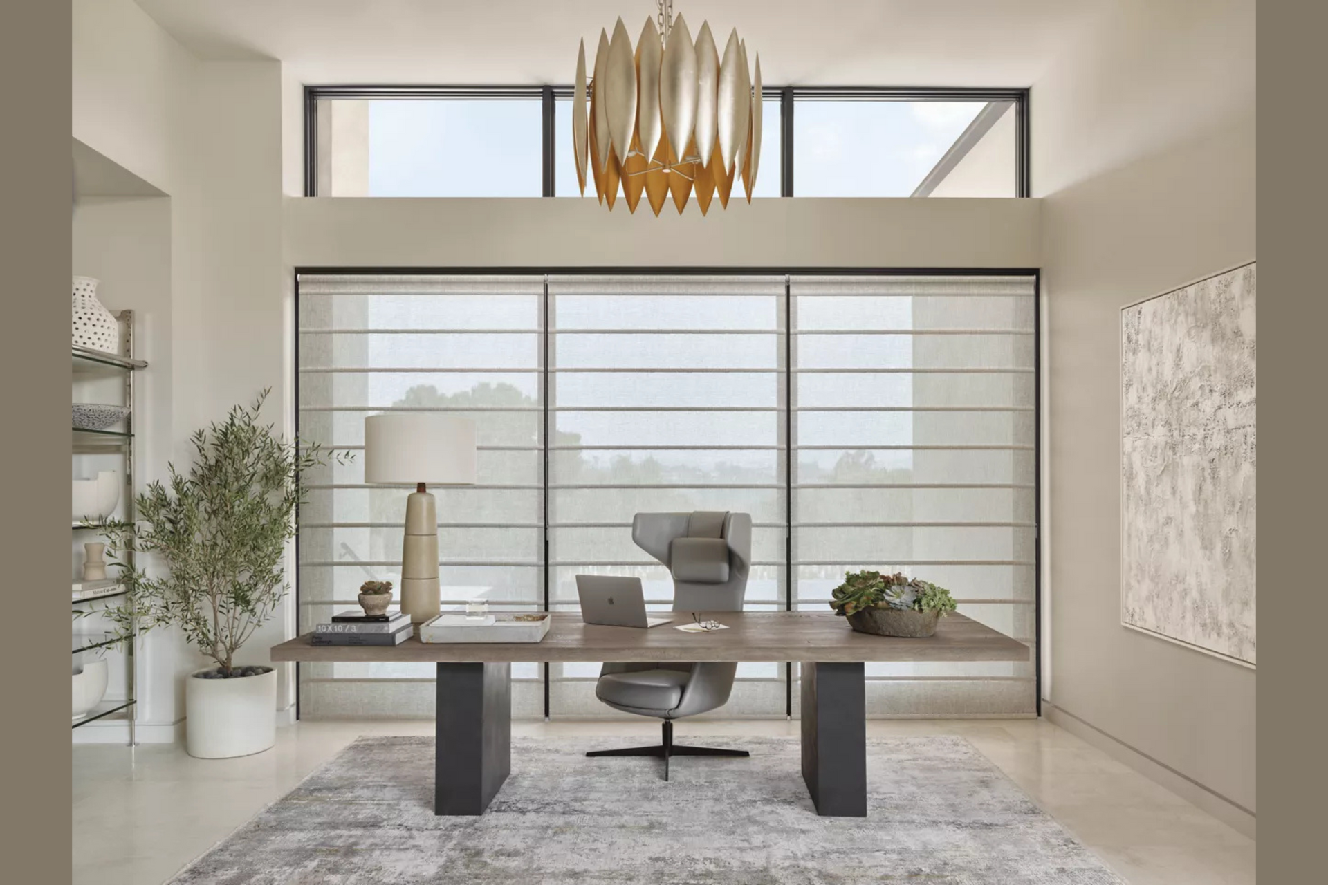 Modern minimalist home office with a dark desk, chair, rug, large window, and gold chandelier.