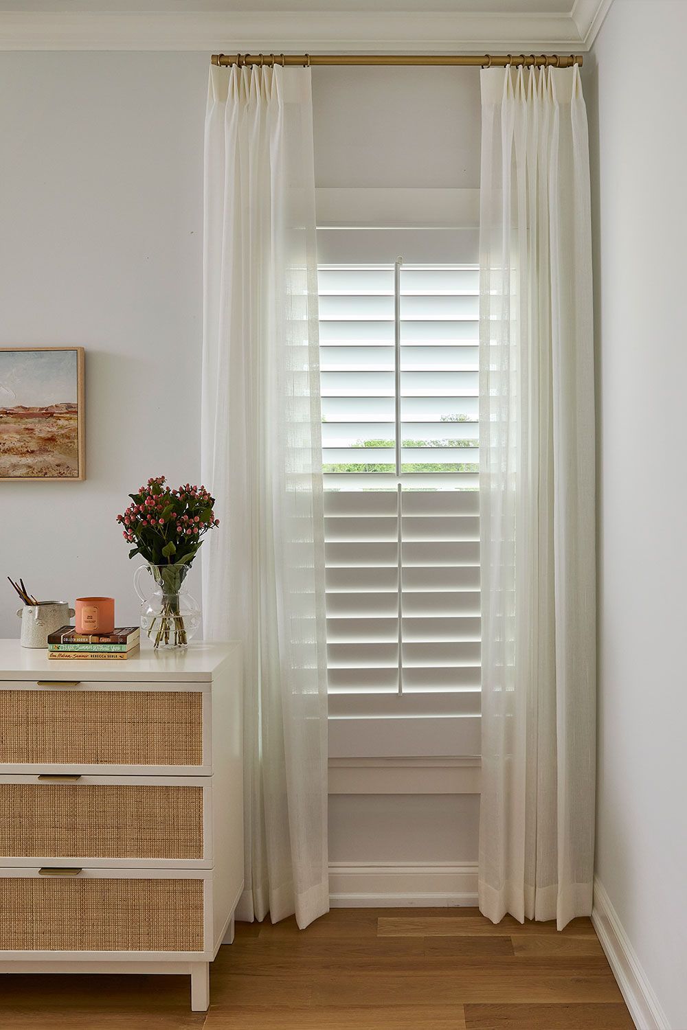 Sheer curtains framing a window with white plantation shutters in a bright room