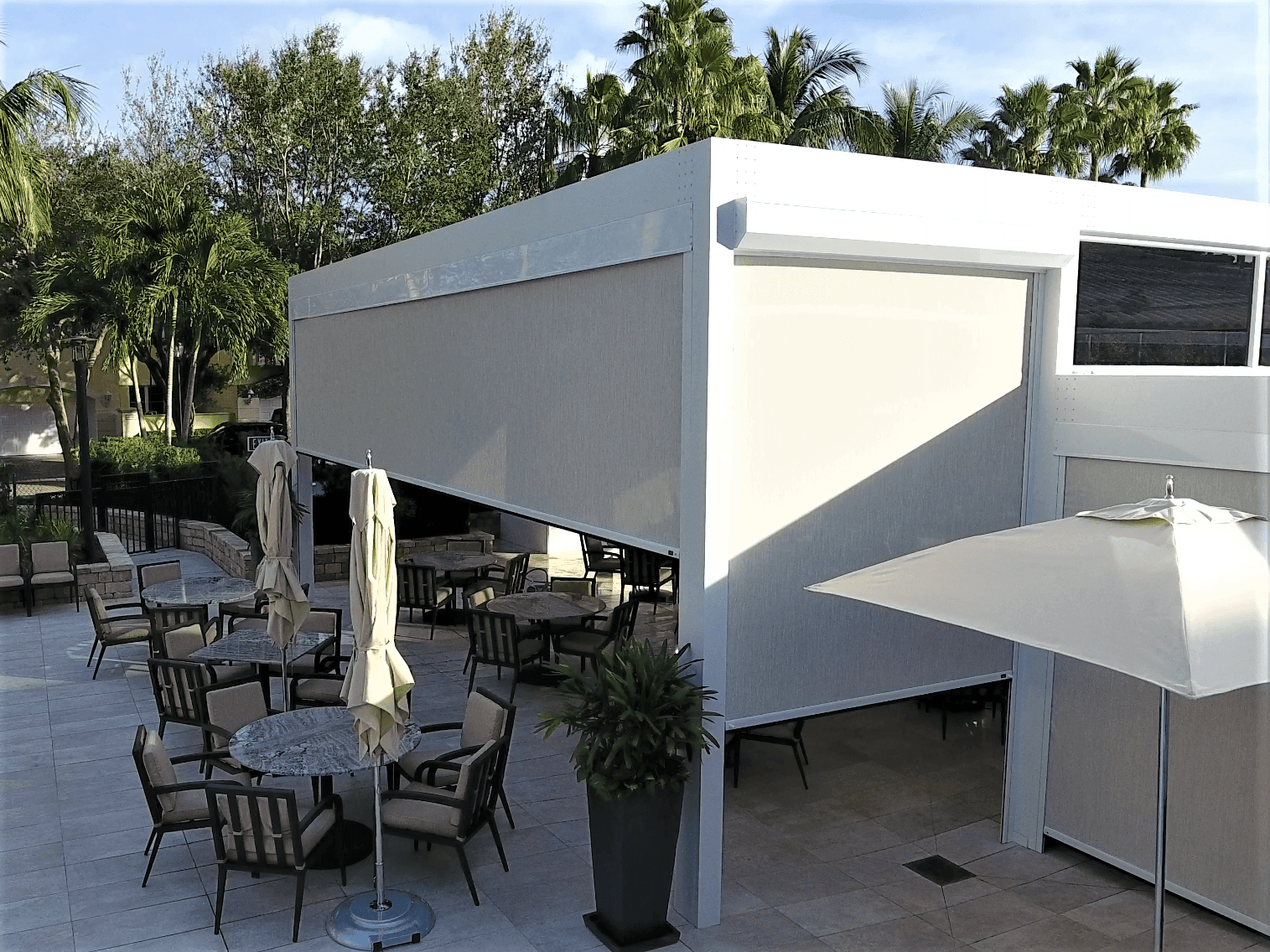 Outdoor patio with tables, chairs, umbrellas, and white canopy seating beside a building