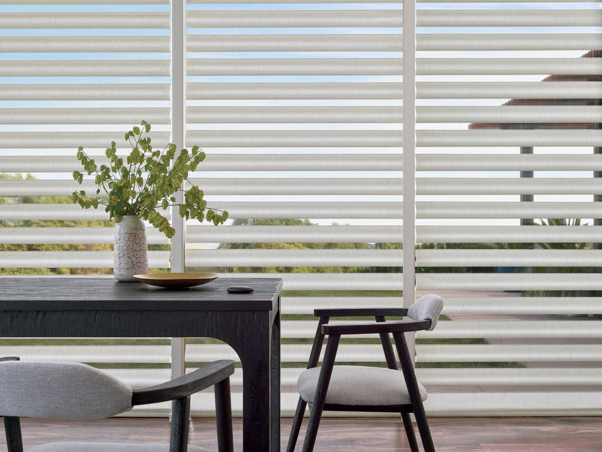 Modern patio with table, chair, potted plant, and striped white privacy screen by the water.