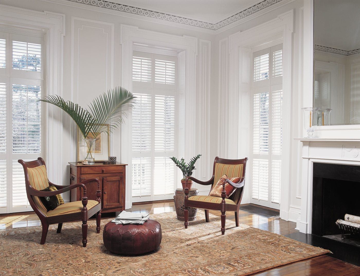Bright living room with two wicker chairs, a small table, tall windows, and a fireplace on the right.