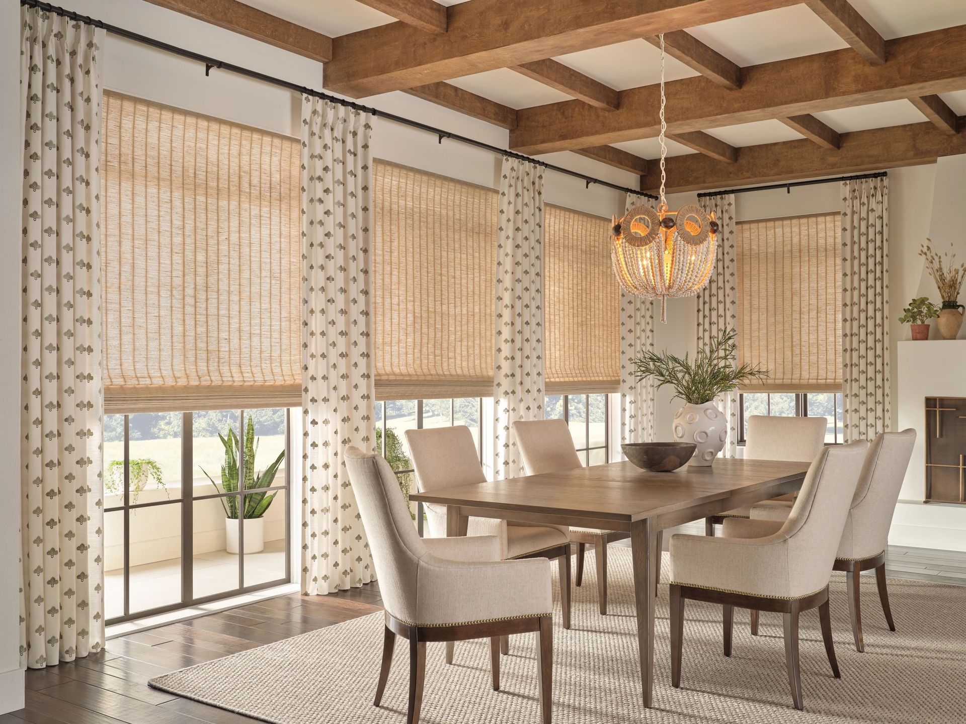 Bright dining room with beige chairs, wooden table, patterned blinds, and a chandelier under exposed beams