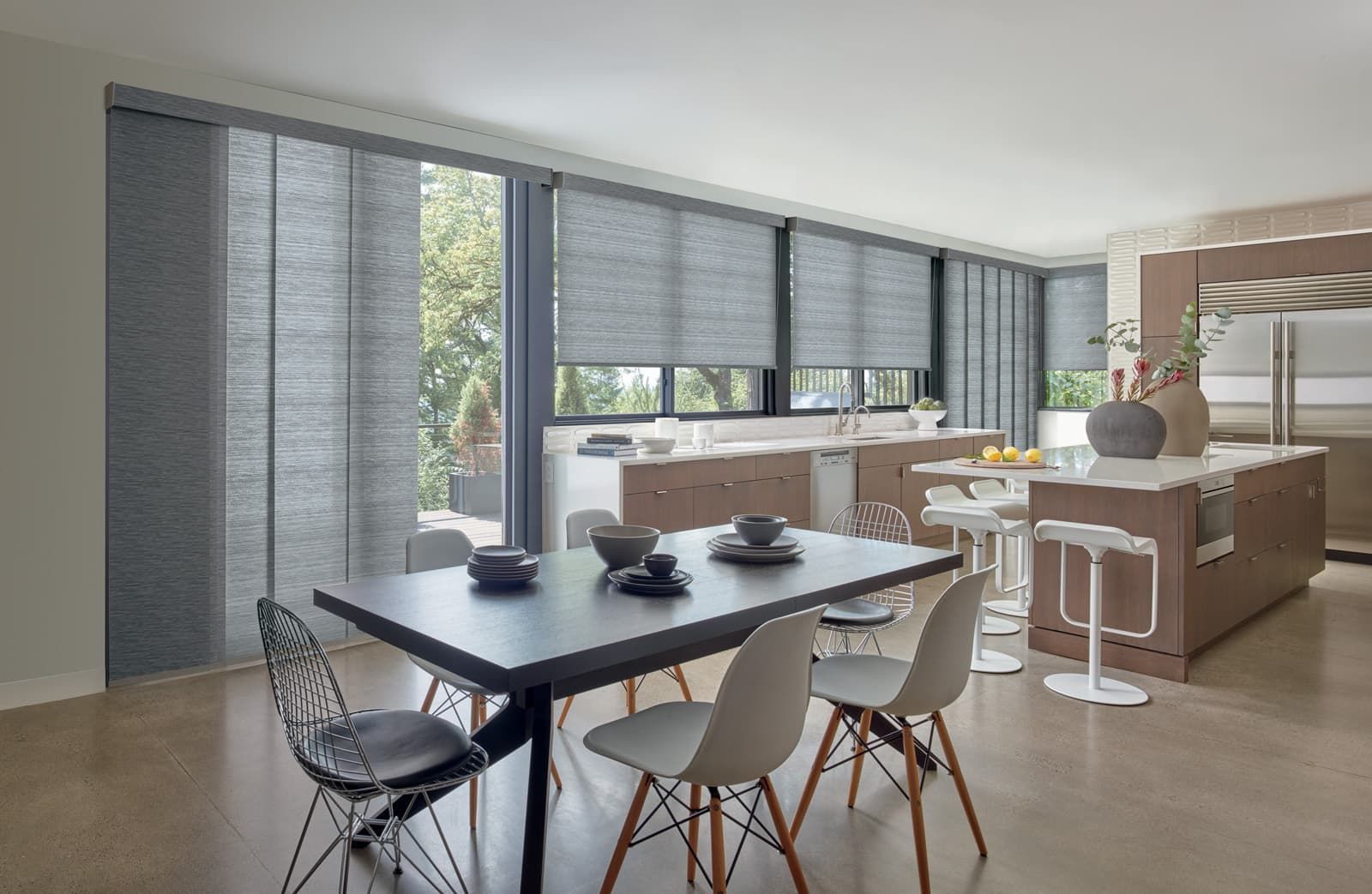 Modern dining area with a dark table, molded chairs, large windows, and a living room beyond