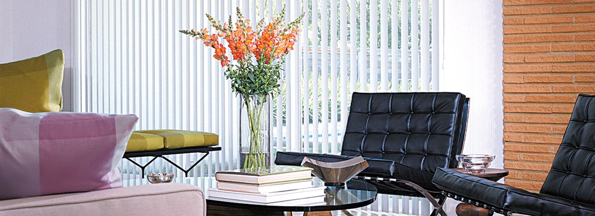 Modern living room with black chairs, a white coffee table, and a vase of orange flowers by vertical blinds.