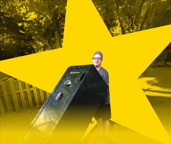 A person holding a large black safe in front of a bright yellow star graphic with a blurred outdoor background.