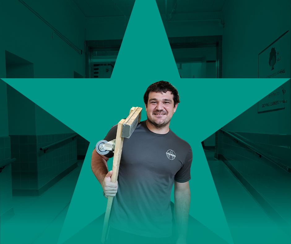 Man holding device over shoulder in a green star, standing in what appears to be a lab.