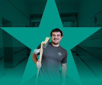 A smiling person wearing a gray shirt stands in a hallway, holding a floor-cleaning tool over their shoulder.