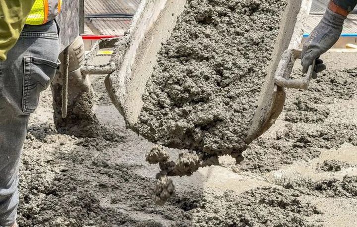 Workers pour wet concrete from a mixer into a construction site form.