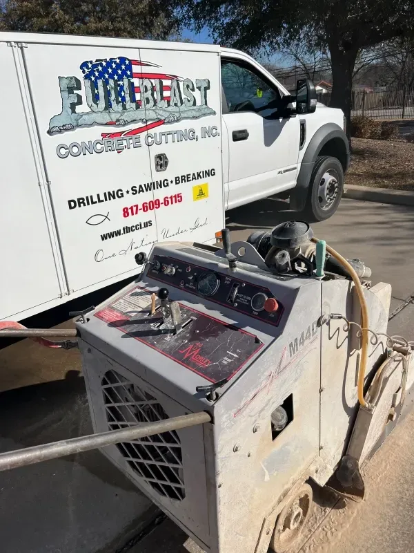 A concrete saw sits in front of a white work van labeled 