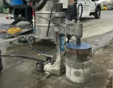 A core drill machine on wheels is being used to cut a circular sample out of a concrete surface outdoors.