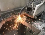 A machine cuts through concrete, creating a bright spray of sparks in an industrial setting.
