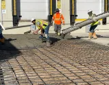 Construction workers in high-visibility gear pour wet concrete over a steel rebar grid at a building site.